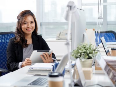 Portrait of pretty Filipino business woman sitting at her table with tablet computer