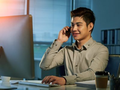 Smiling  young Filipino businessman talking on phone in dark office